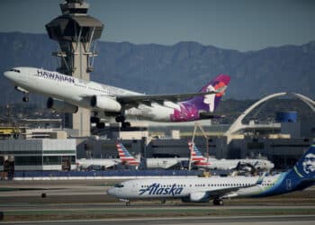 Hawaiian Airlines plane takes off while Alaska Airlines plane sits on tarmac